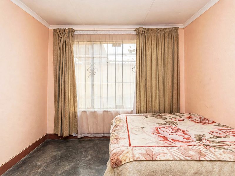 A bedroom featuring security bars on the window, coving, and skirting boards, with dated wall finishes and flooring in need of updating.