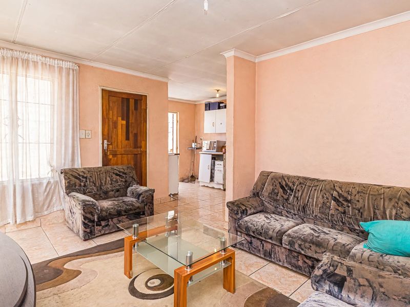 Open plan living area featuring tiled flooring and coved ceilings, with an adjacent kitchen area visible in the background.