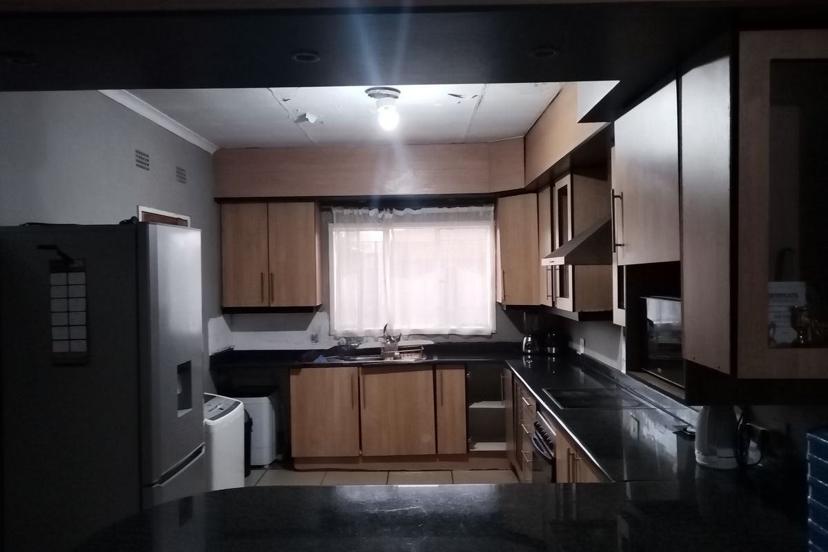 A functional kitchen featuring wood-finish cabinetry, dark granite countertops, and integrated appliances, currently showing signs of wear on the ceiling and cabinetry.