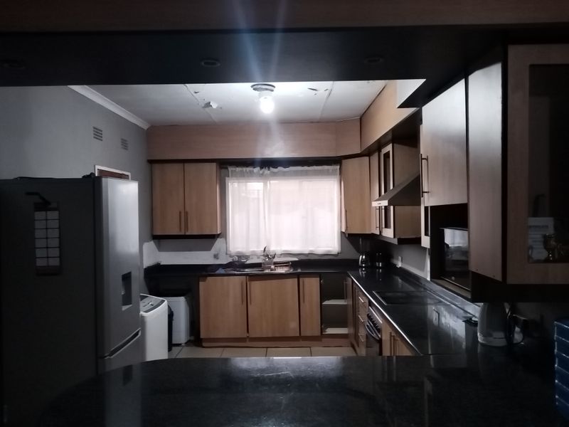 A functional kitchen featuring wood-finish cabinetry, dark granite countertops, and integrated appliances, currently showing signs of wear on the ceiling and cabinetry.