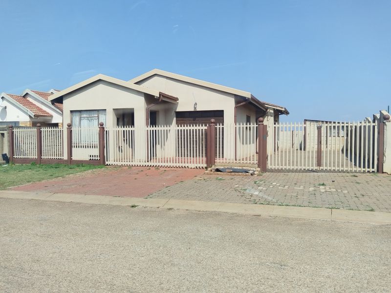 Front view of a single-story residential house featuring a paved driveway, perimeter fencing with a sliding gate, and an integrated single garage.