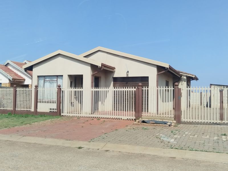 Front view of a single-story house featuring a paved driveway, secure metal fencing, and an integrated garage.