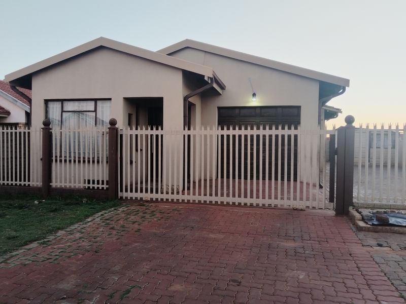 Front view of a single-story house featuring a paved driveway, secure metal fencing, and an integrated garage.