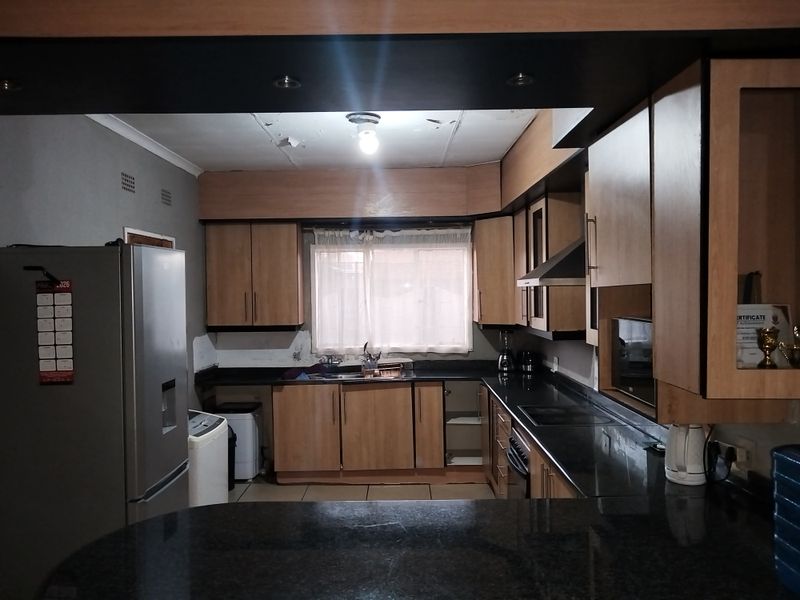 A dated kitchen featuring laminate cabinetry, granite countertops, and built-in appliances, currently showing signs of wear including ceiling damage and missing cabinet hardware.
