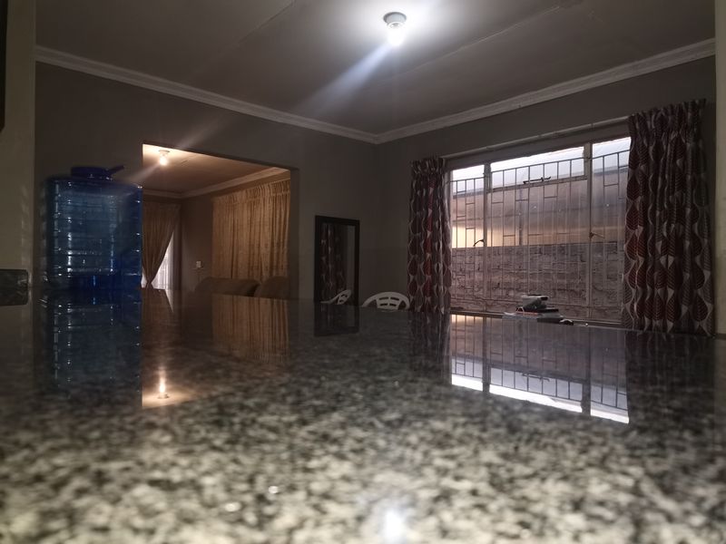A kitchen interior featuring a polished granite countertop, security bars on the window, and crown molding, viewed in low-light conditions.