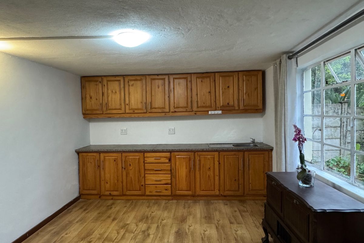 A functional kitchen area featuring wooden cabinetry, granite countertops, a stainless steel sink, and laminate flooring with natural light from large windows.