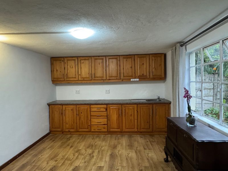A functional kitchen area featuring wooden cabinetry, granite countertops, a stainless steel sink, and laminate flooring with natural light from large windows.