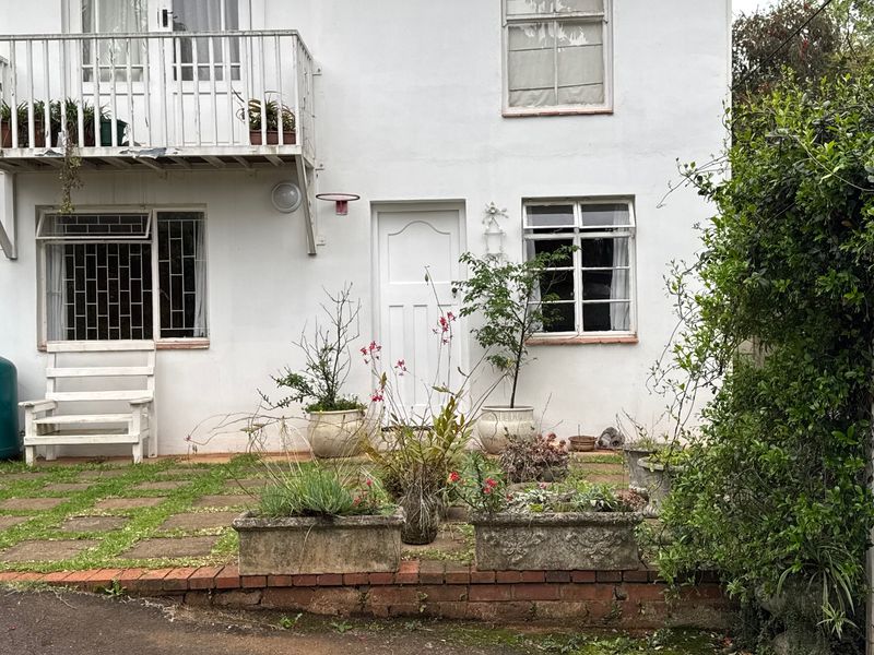 Rear exterior view of the cottage featuring a paved patio area, a small balcony with metal railings, and white painted masonry walls.