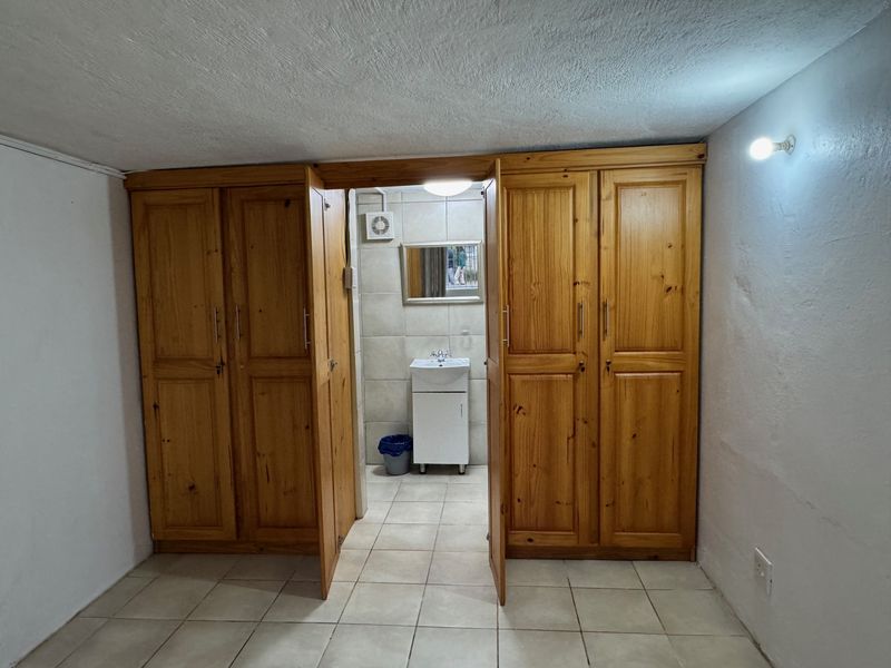 A bedroom featuring built-in wooden wardrobes and direct access to an en-suite bathroom with a vanity basin and extractor fan.