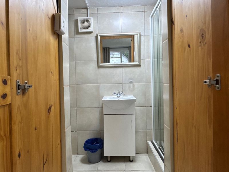 Compact bathroom featuring a vanity basin, shower enclosure, and tiled finishes, framed by timber doors.
