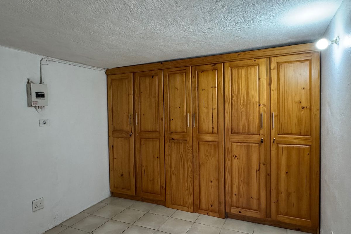 A functional bedroom space featuring extensive built-in wooden cabinetry, tiled flooring, and an exposed electrical distribution board on the wall.