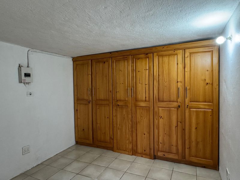 A functional bedroom space featuring extensive built-in wooden cabinetry, tiled flooring, and an exposed electrical distribution board on the wall.