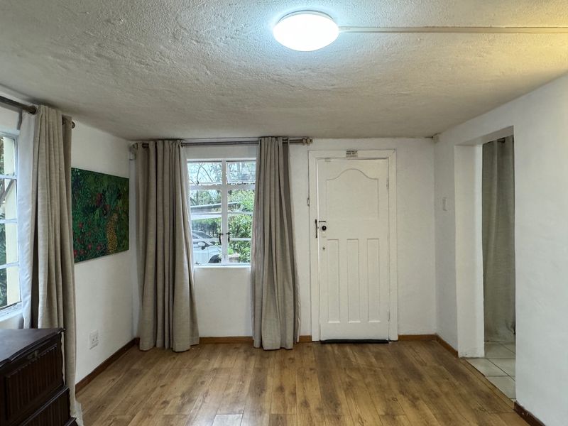 A bright, empty living room featuring laminate flooring, timber-framed windows, and a classic panelled entrance door, offering a neutral canvas for interior design.