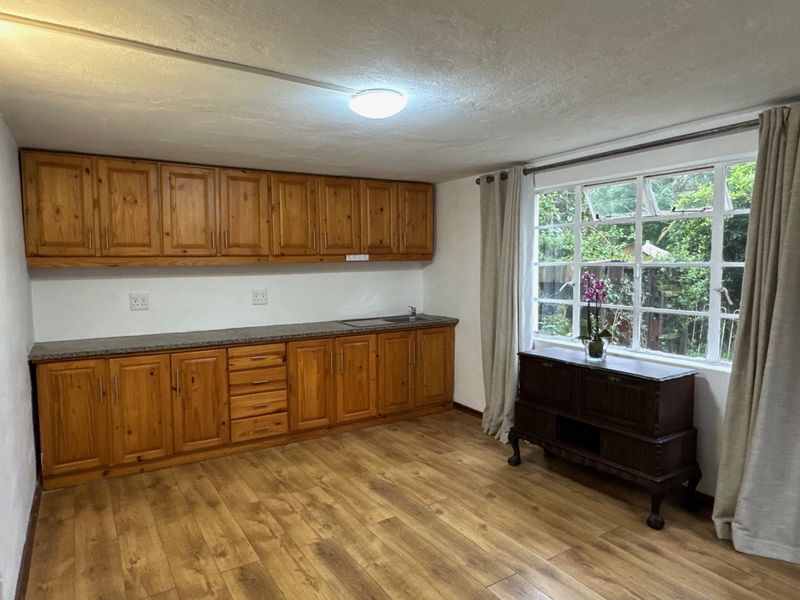 A functional kitchen featuring warm-toned wooden cabinetry, laminate countertops, and durable laminate flooring, with natural light provided by a large multi-pane window.