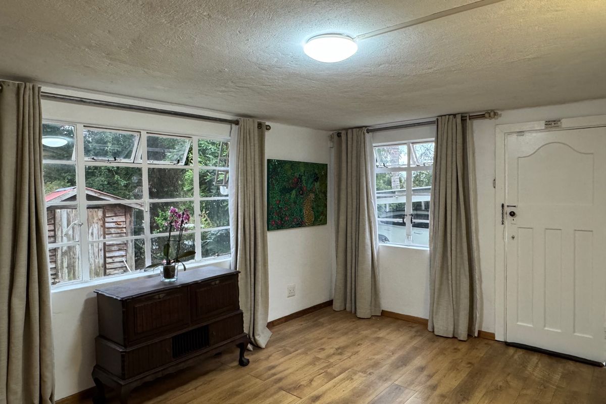 A living room featuring laminate flooring, steel-framed windows, and a panelled entrance door, offering a functional space with potential for cosmetic updates.