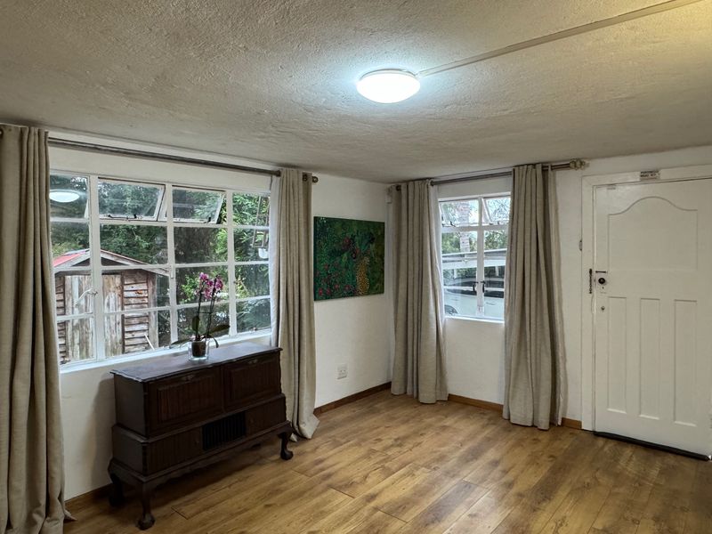 A living room featuring laminate flooring, steel-framed windows, and a panelled entrance door, offering a functional space with potential for cosmetic updates.