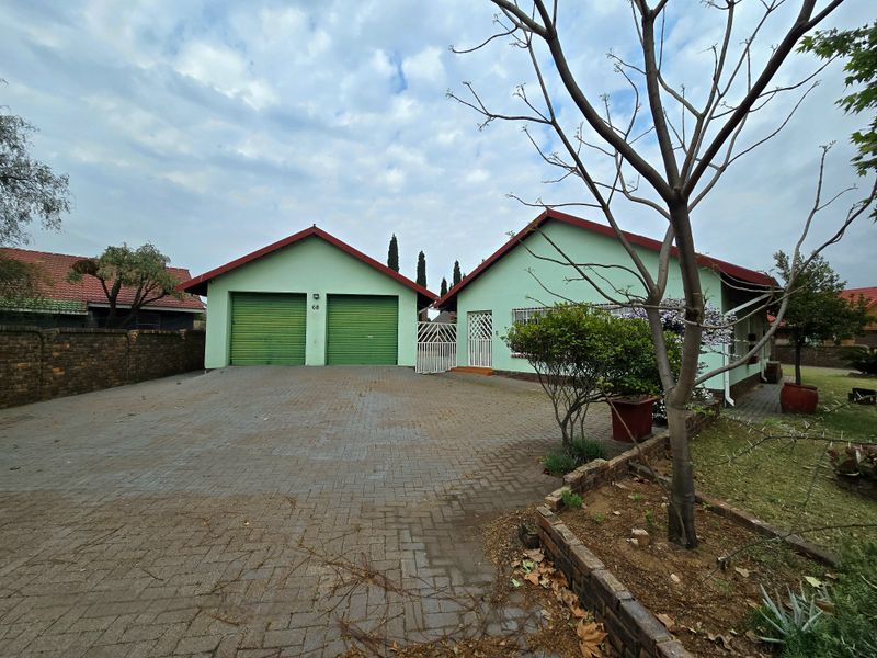 Front view of a residential property featuring a double garage, paved driveway, and secure gated entrance with a brick boundary wall.