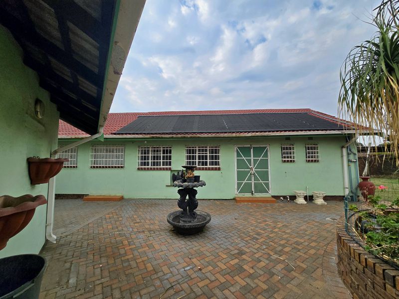 Rear exterior view of the house featuring a paved courtyard, solar panels on the roof, and security bars on the windows.