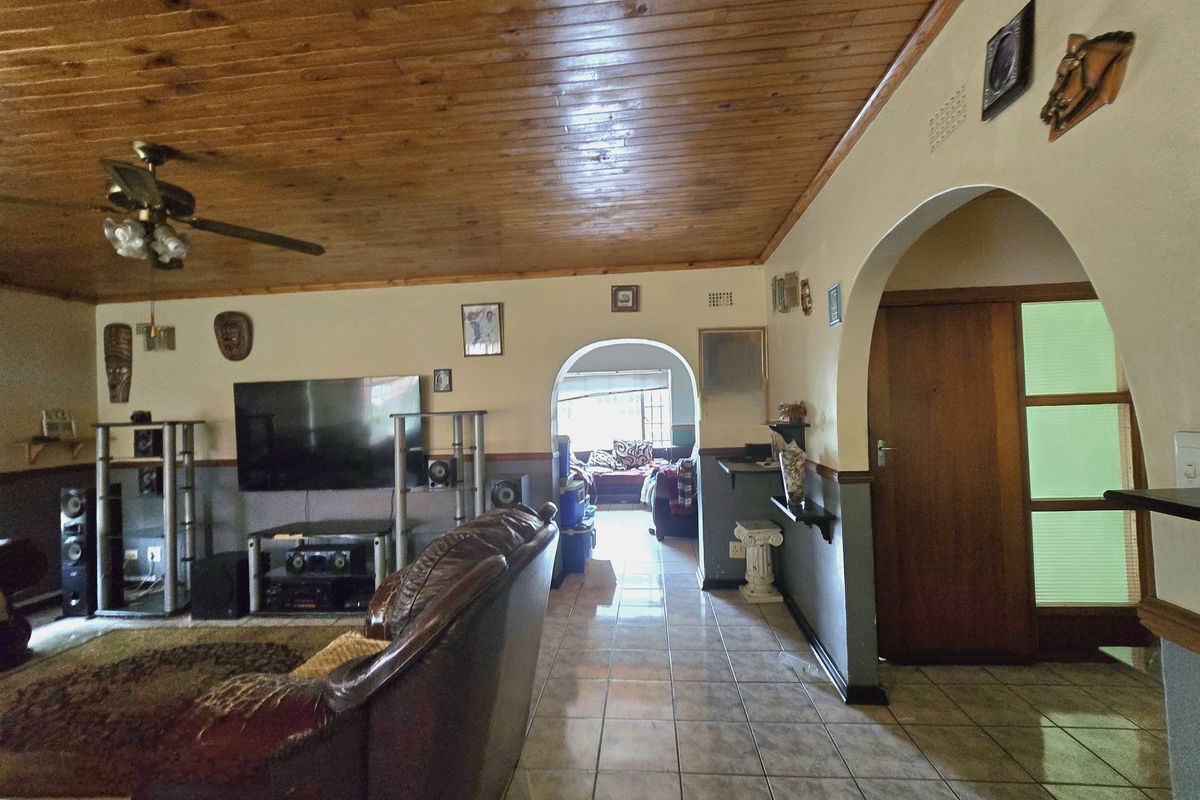 Spacious living area featuring a timber tongue and groove ceiling, ceramic tiled flooring, and distinctive arched doorways connecting to adjacent rooms.