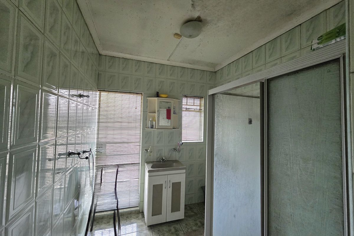 A dated bathroom featuring a vanity basin, shower enclosure, and full-height wall tiling. The ceiling shows signs of significant wear and staining.