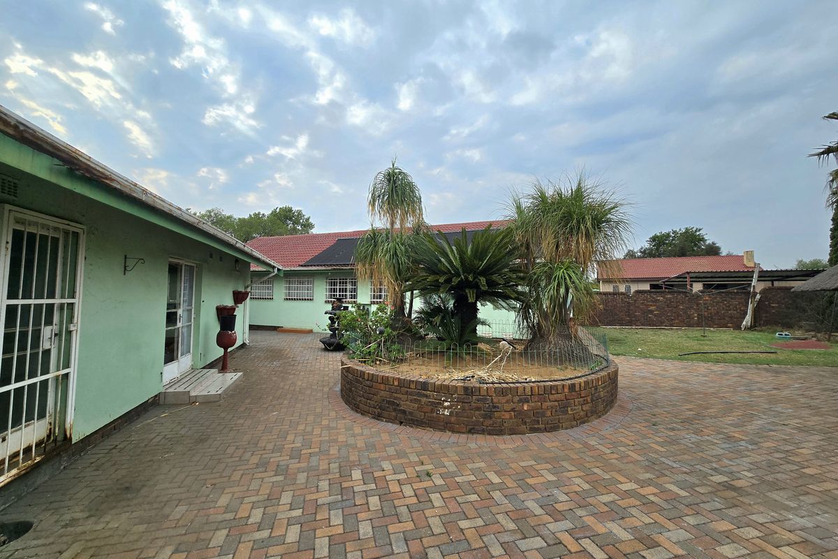 Rear exterior view featuring a brick-paved courtyard, a central raised garden bed, and a secure perimeter wall.
