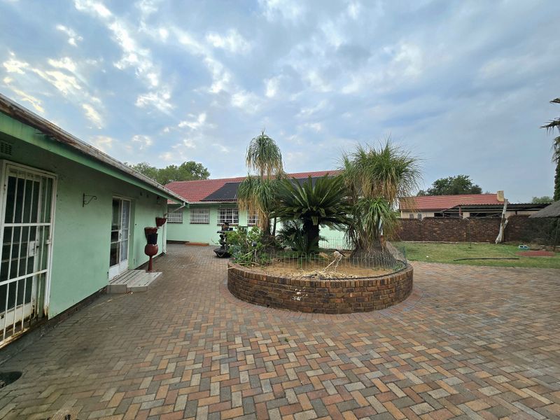 Rear exterior view featuring a brick-paved courtyard, a central raised garden bed, and a secure perimeter wall.