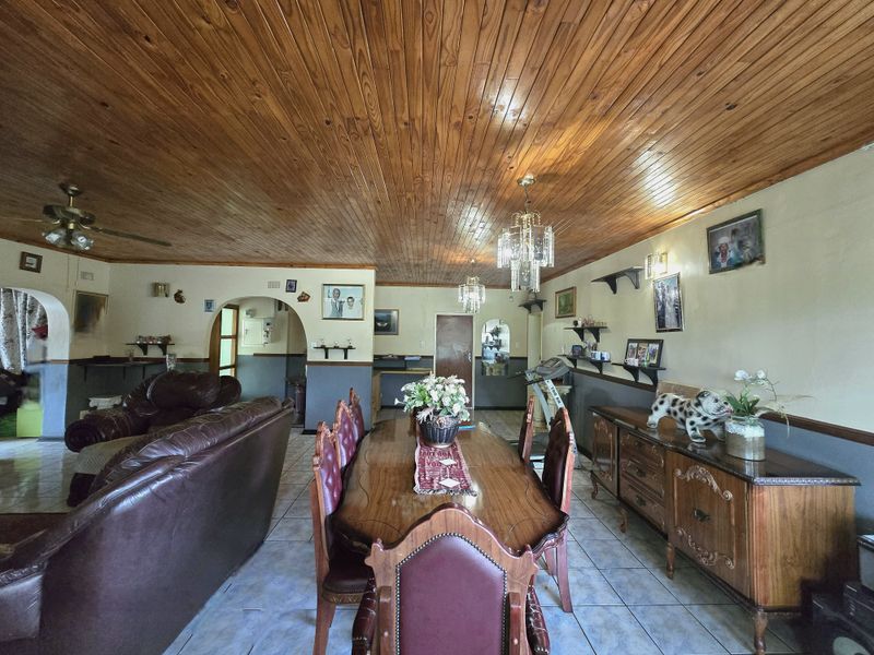 Spacious open-plan living and dining area featuring a distinctive timber tongue and groove ceiling, ceramic tiled flooring, and classic archway transitions.