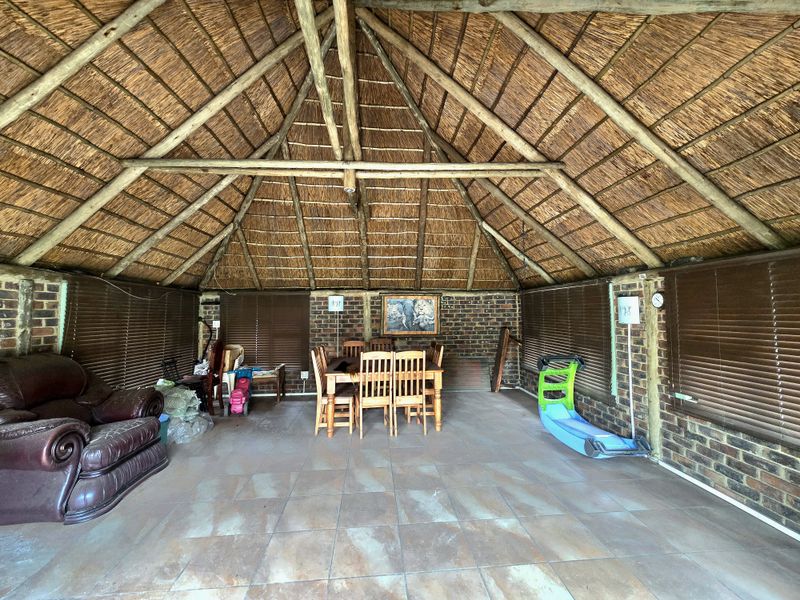 Spacious covered patio featuring a traditional thatched roof, exposed brick walls, and tiled flooring, offering a rustic outdoor entertainment area.
