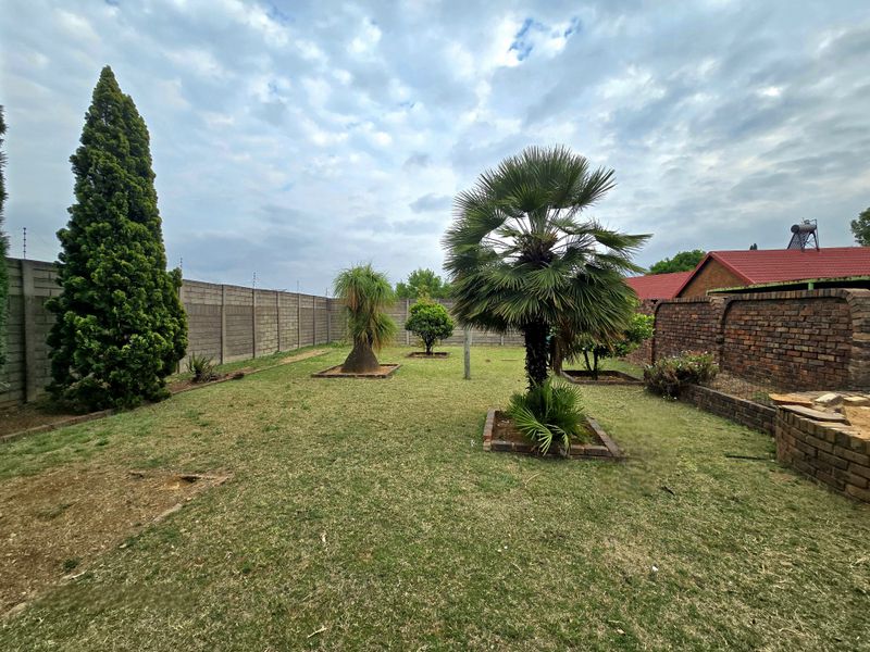 A spacious backyard featuring a lawn, established palm trees, and secure perimeter walling with electric fencing.