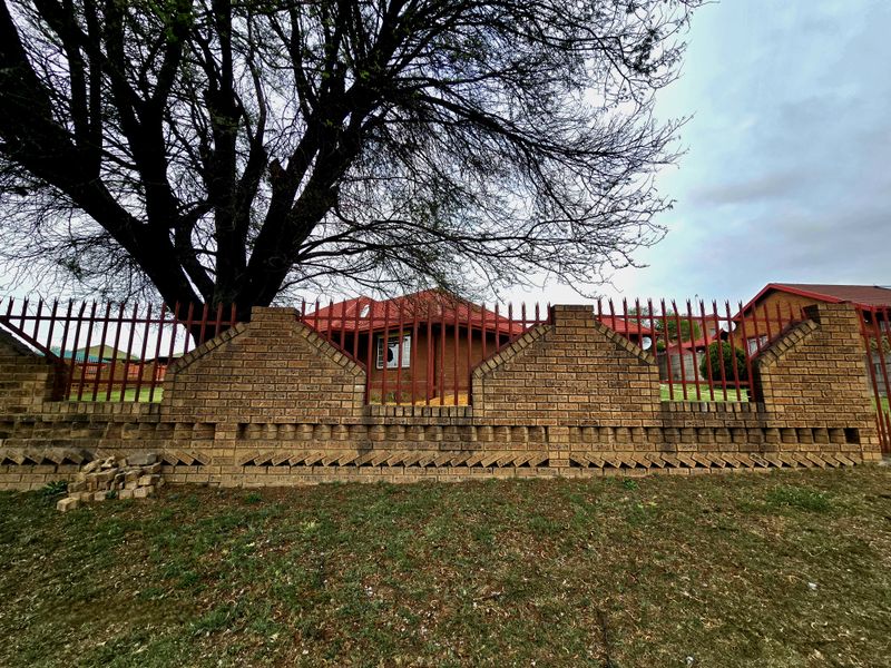 Front view of a face brick house featuring a secure boundary wall with steel palisade fencing and a tiled roof.