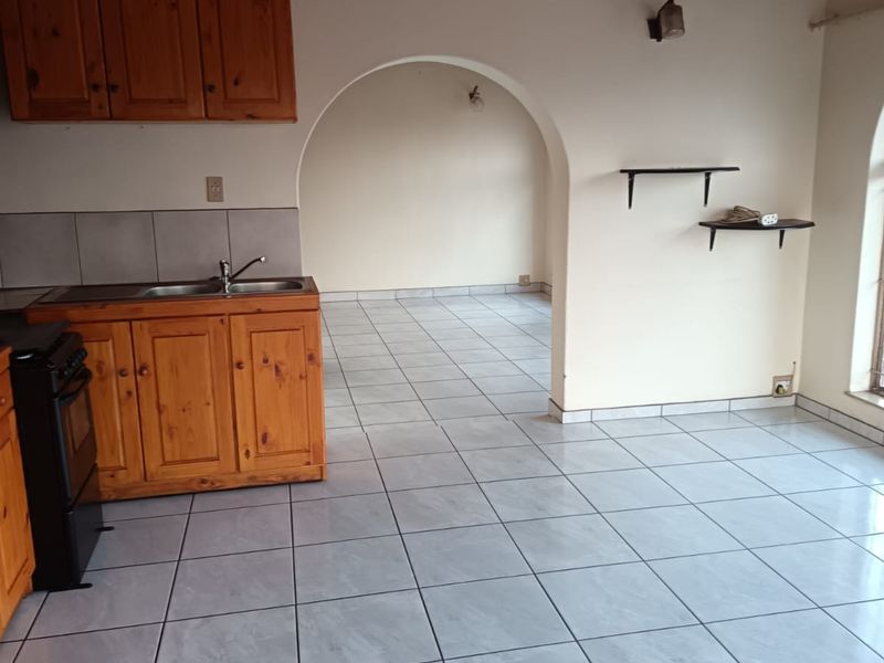 Open plan kitchen area featuring tiled floors, wooden cabinetry, and a distinctive arched doorway leading to an adjacent living space.