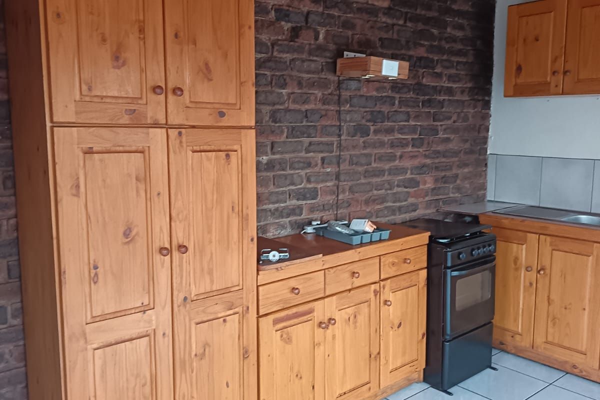 A functional kitchen featuring timber cabinetry, an exposed brick wall, timber ceiling, and tiled flooring, offering a rustic aesthetic with potential for modernization.