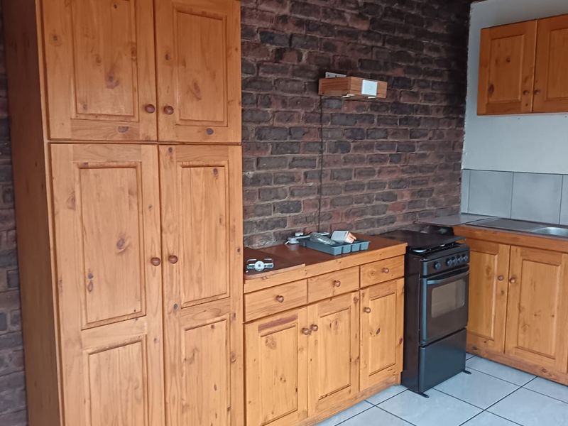 A functional kitchen featuring timber cabinetry, an exposed brick wall, timber ceiling, and tiled flooring, offering a rustic aesthetic with potential for modernization.