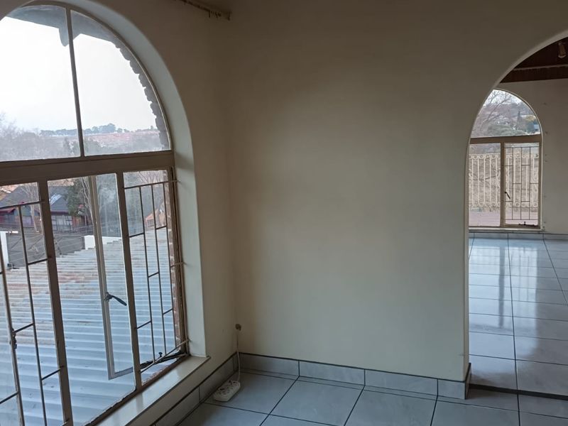 An empty living area featuring arched windows, tiled flooring, and a timber ceiling, offering a bright and open space with views.