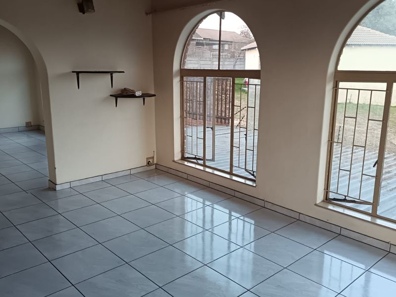 Spacious living area featuring arched windows with security bars, polished tiled flooring, and a timber ceiling with an integrated fan.