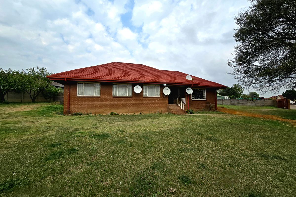 A detached single-story brick house featuring a prominent red tiled roof, metal-framed windows, and a large surrounding lawn area.