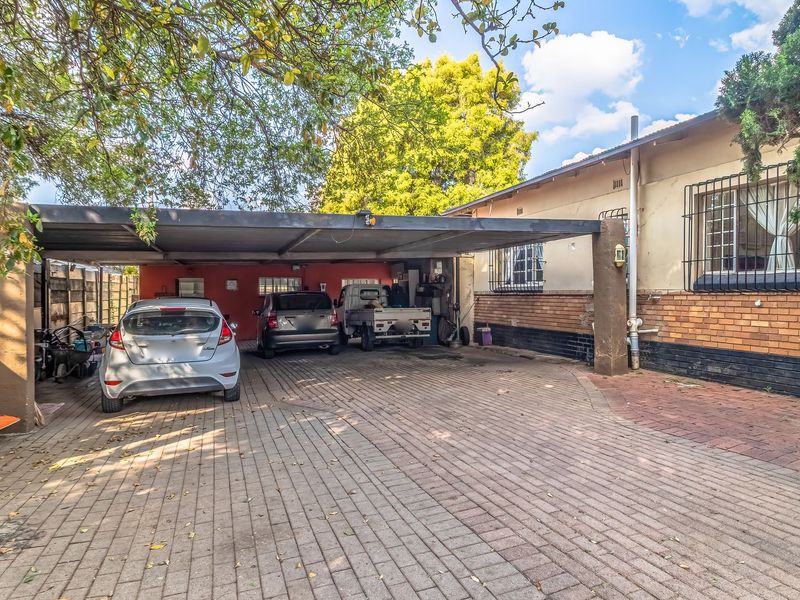 A paved driveway leading to a covered carport area attached to the side of the house, featuring brick exterior walls and security window bars.