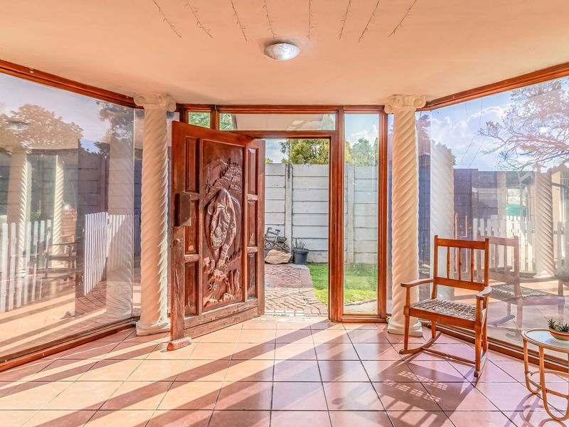 A bright entrance foyer featuring a decorative carved wooden door, classic columns, and extensive glass paneling that provides a seamless transition to the outdoors.