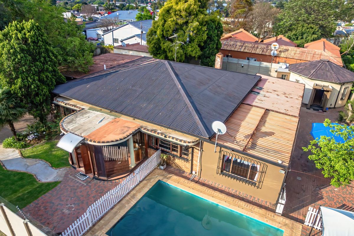 Aerial view of the property featuring a swimming pool, brick paved patio area, and a corrugated metal roof structure.