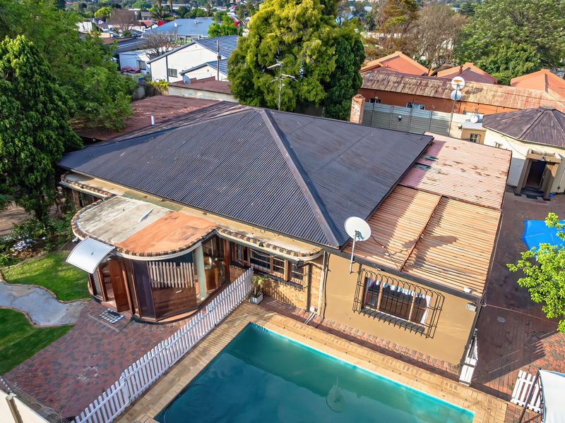 Aerial view of the property featuring a swimming pool, brick paved patio area, and a corrugated metal roof structure.