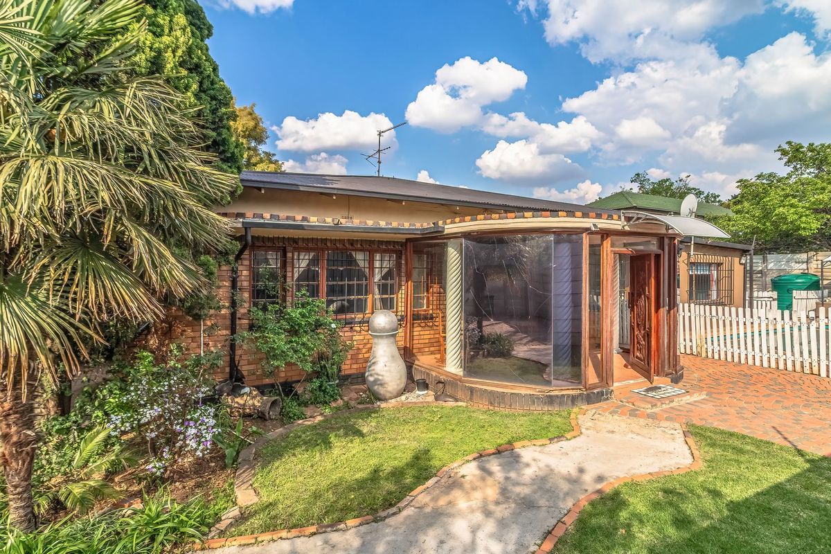 Rear view of the property featuring a brick facade, a unique curved glass sunroom, a paved patio area, and a well-maintained garden with a picket fence.