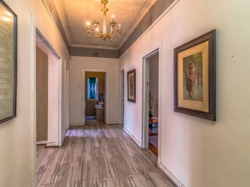 A spacious hallway featuring a decorative pressed metal ceiling, classic chandelier lighting, and modern timber-look flooring, providing access to multiple rooms.