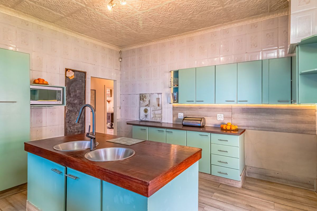 A functional kitchen featuring light blue cabinetry, a central island with a wooden countertop, double sinks, and tiled wall finishes.