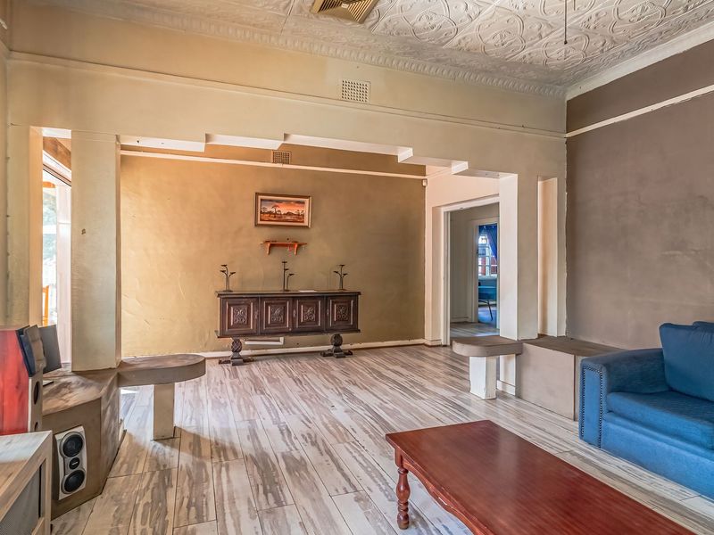 Spacious living area featuring a decorative pressed metal ceiling, built-in concrete shelving, and timber-look flooring, offering a unique architectural foundation for renovation.