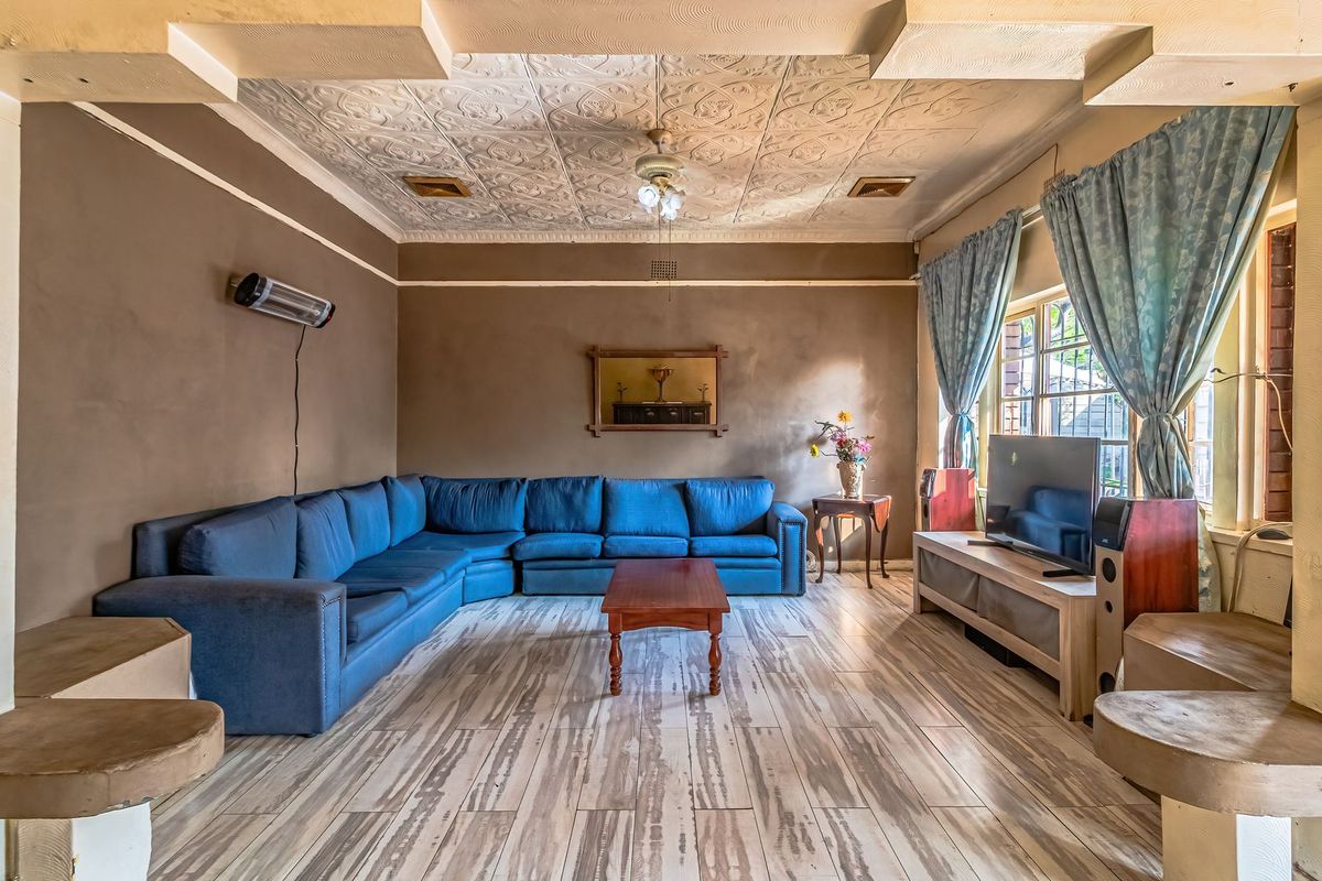 Spacious living room featuring a decorative pressed metal ceiling, tiled flooring, and a wall-mounted heater, offering a classic architectural aesthetic.