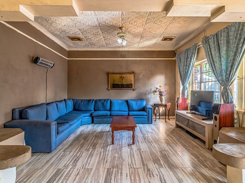 Spacious living room featuring a decorative pressed metal ceiling, tiled flooring, and a wall-mounted heater, offering a classic architectural aesthetic.