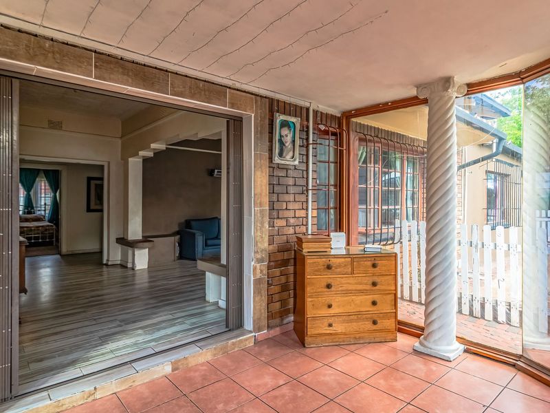 A covered patio area featuring tiled flooring, exposed brickwork, and a decorative column, providing a transition space between the interior living area and the outdoors.