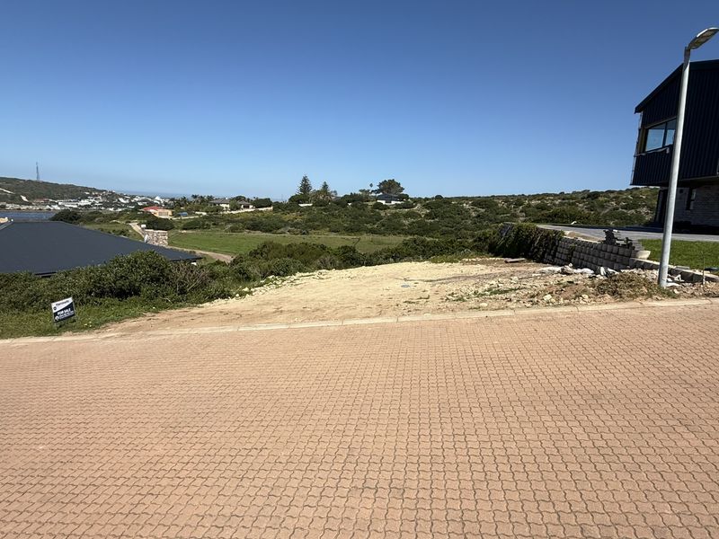 A vacant residential plot featuring a paved driveway, street lighting, and a retaining wall, offering scenic views of the surrounding landscape.