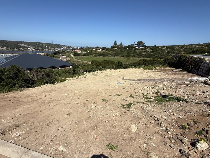 A vacant residential plot featuring a retaining wall and views of the surrounding landscape and nearby coastal area.