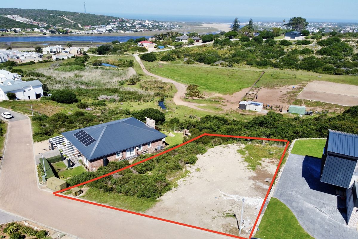 Aerial view of a vacant residential plot outlined in red, situated in a coastal estate with surrounding natural landscape and nearby residential properties.